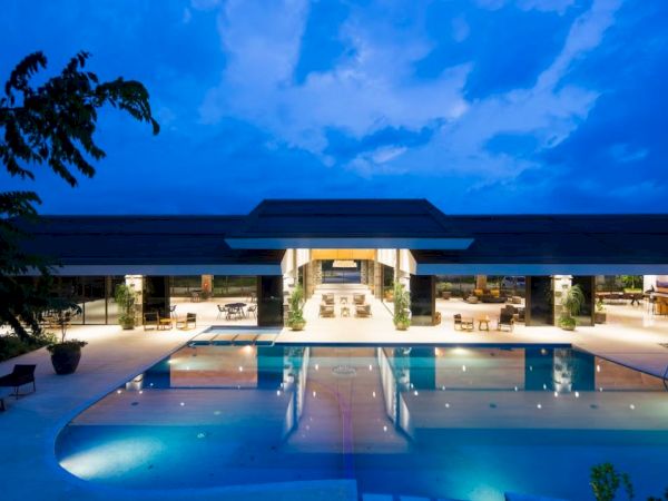 A luxurious resort with a large illuminated pool and open lounge area under a cloudy evening sky.