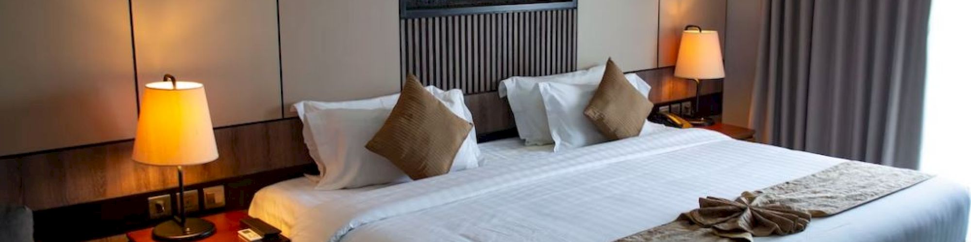 A modern hotel room with a large bed, two bedside lamps, and a decorative wall feature. The room looks cozy and inviting.