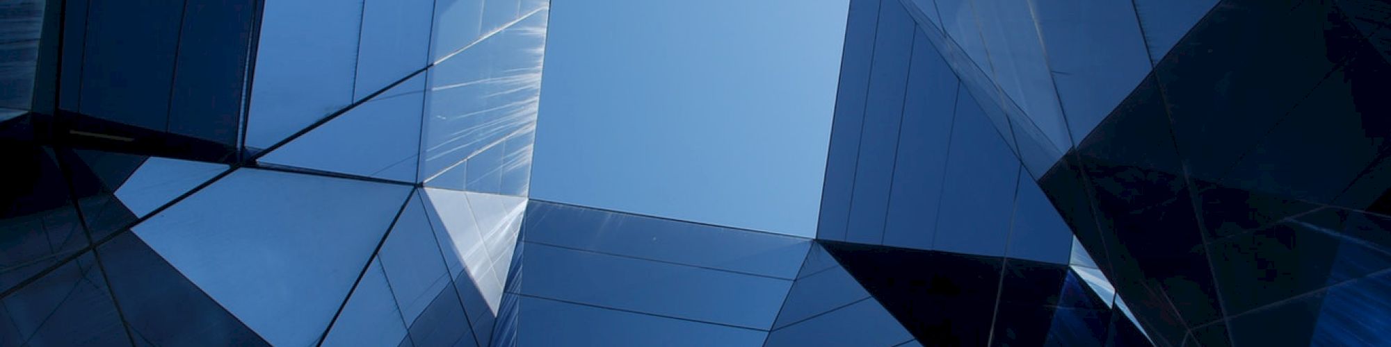 Abstract architecture with reflective glass panels creating geometric patterns against a blue sky, forming a unique visual effect.