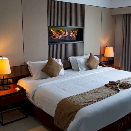 A cozy hotel room features a large bed with decorative pillows, bedside lamps, and a window with curtains, creating a relaxing ambiance.
