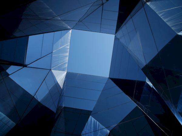 The image shows an upward view of glass buildings forming a geometric pattern, reflecting a blue sky at the center.