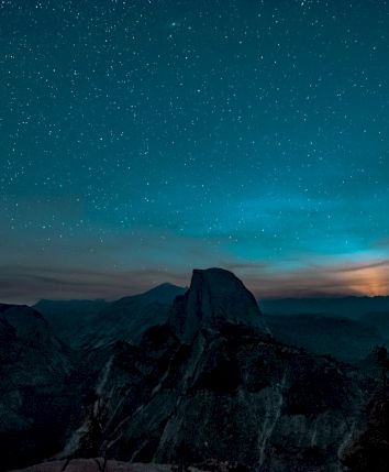 A starry sky over a mountainous landscape, with a glowing horizon partially illuminating the scene.