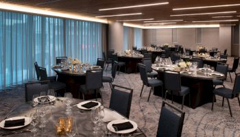 A banquet hall with round tables set for dinner, featuring elegant tableware, black napkins, and decorative floral centerpieces.
