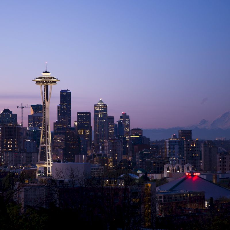 Seattle skyline at dusk with Space Needle and city buildings, set against Mount Rainier's silhouette in the distance.