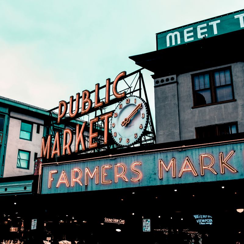The image shows a market building with signs reading "Public Market" and "Farmers Market," featuring a large clock on the facade.