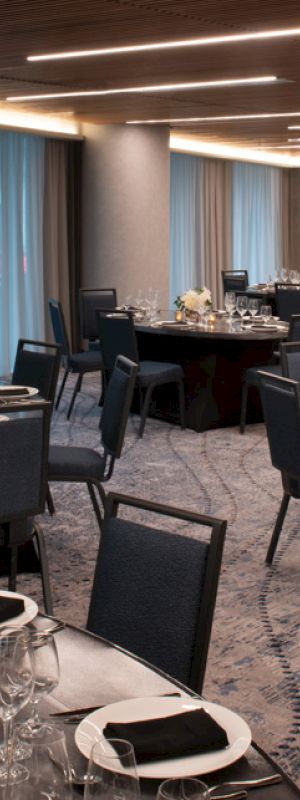 An elegant banquet hall set with round tables, chairs, glassware, and floral centerpieces, ready for an event or gathering.
