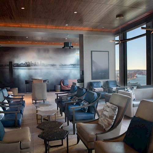 A modern lounge with elegant seating, large windows offering city views, stylish decor, and ambient lighting creates a cozy atmosphere.