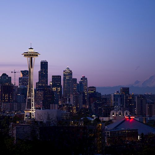 Seattle skyline at dusk featuring the Space Needle and Mount Rainier in the background, set against a clear evening sky.