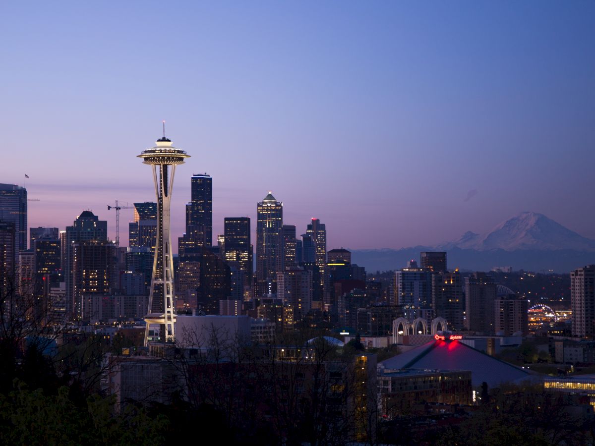 Seattle skyline at dusk with the Space Needle prominently featured and Mount Rainier in the background.