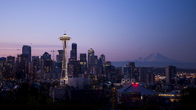 Seattle skyline at dusk with the Space Needle prominently featured and Mount Rainier in the background.
